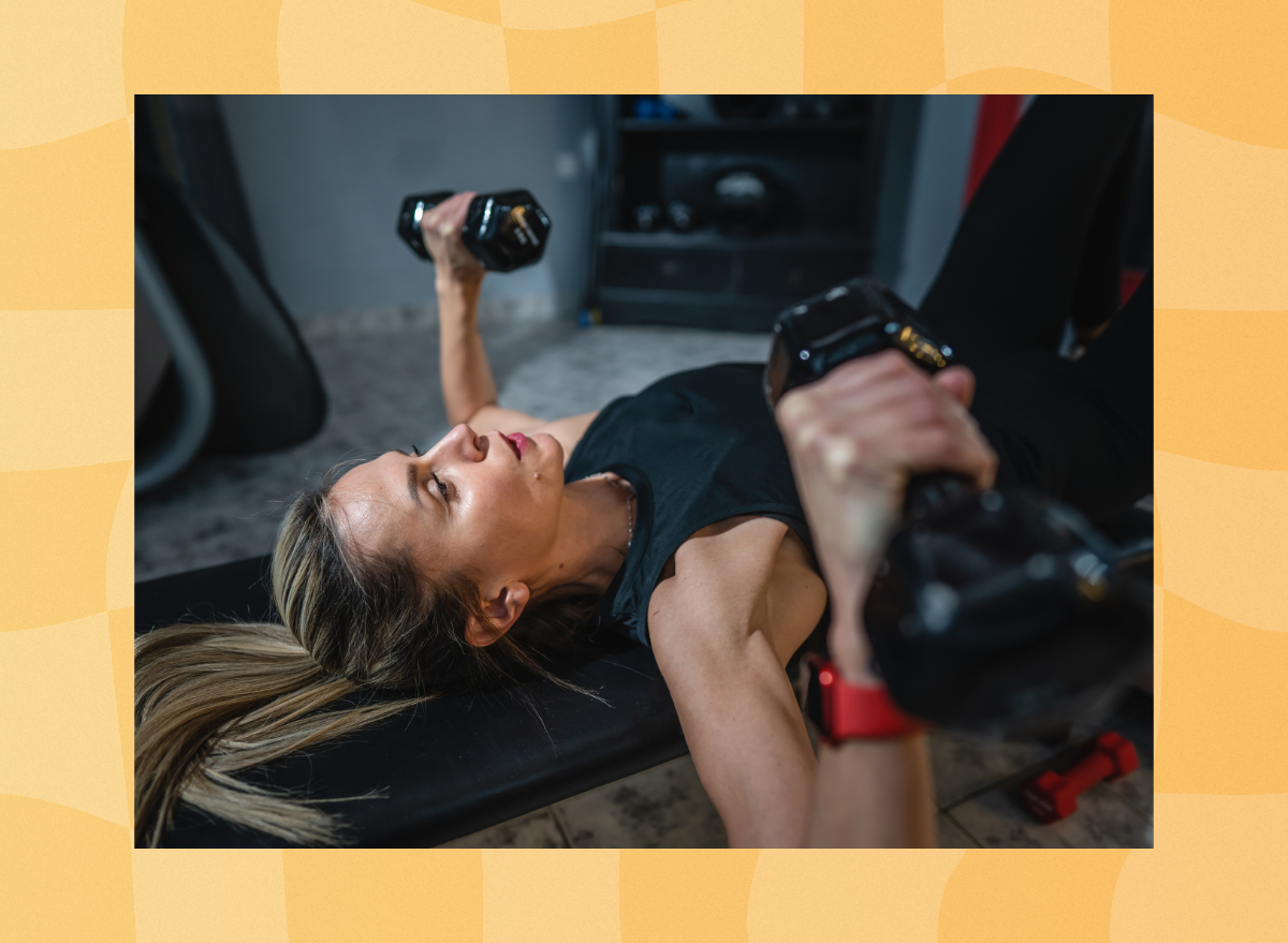 fit, middle-aged woman doing bench press exercise with dumbbells in dark gym