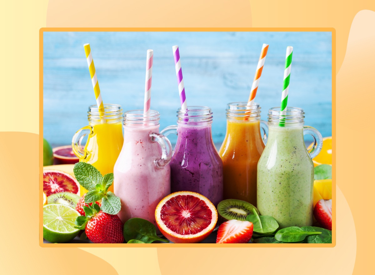 lineup of colorful smoothies with straws in tall mason jars surrounded by fresh fruit