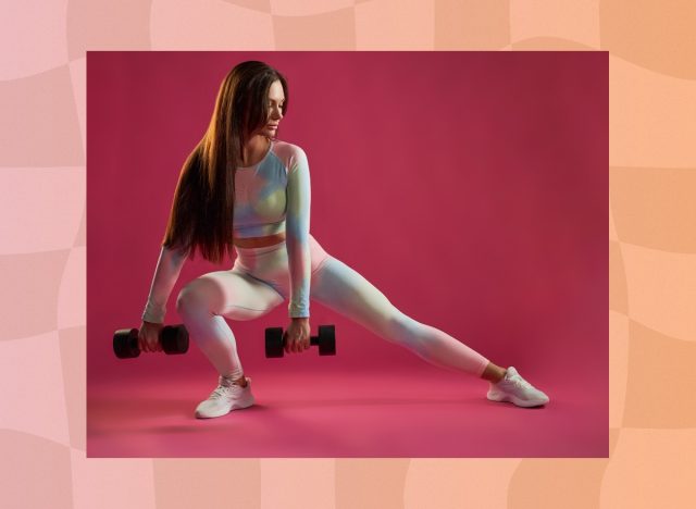 woman doing dumbbell lateral squat in front of dark pink backdrop