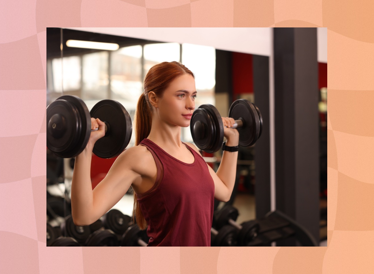 fit, determined red-haired woman doing dumbbell shoulder presses at the gym in the weight room