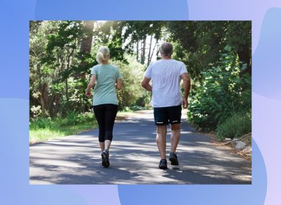 mature couple walking for exercise on path surrounded by trees on sunny day