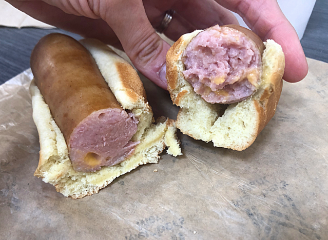 a hand holding a cut in half sam's club cheddar hot dog