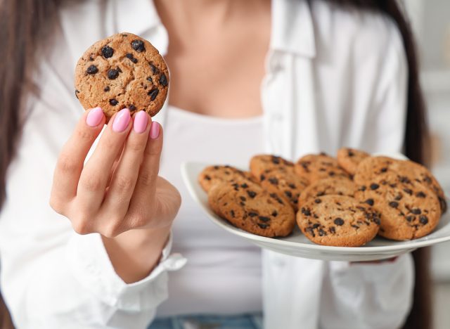 Beautiful young woman holding plate of tasty cookies with chocolate chips at home, closeup