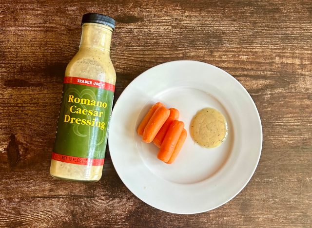 trader joe's romano caesar dressing on a plate with baby carrots next to the bottle of dressing