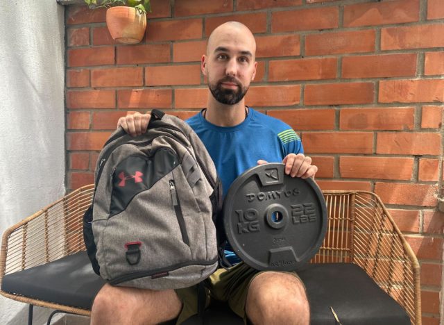 trainer sitting down and holding a backpack and weight plate for rucking