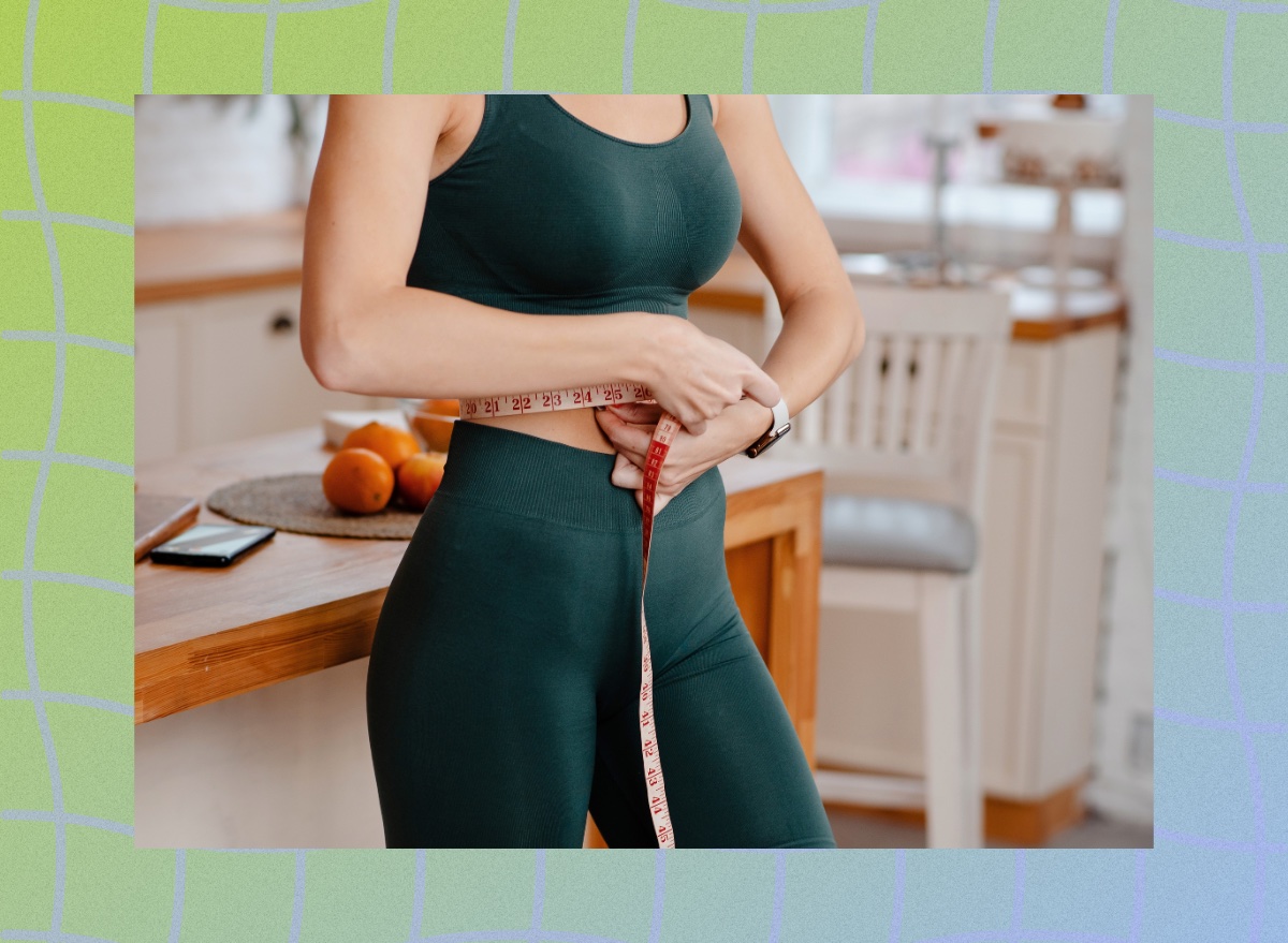 close-up of sporty fitness woman measuring her waistline in kitchen