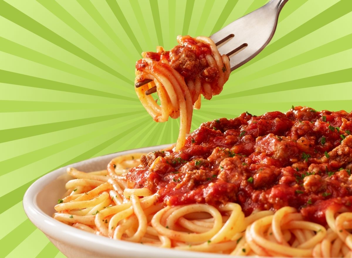 A closeup of red sauce-covered spaghetti, including noodles twirled with a fork, set against a vibrant green background