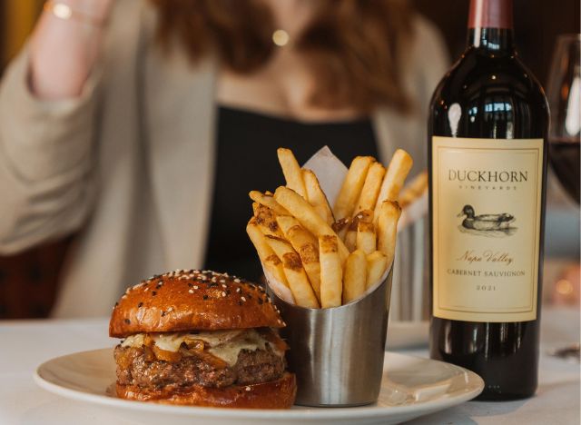 Capital Grille wagyu burger on a table with fries and a bottle of Cabernet Sauvignon