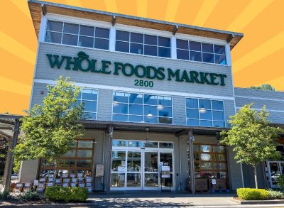 The storefront of a Whole Foods Market set against a vibrant orange background.