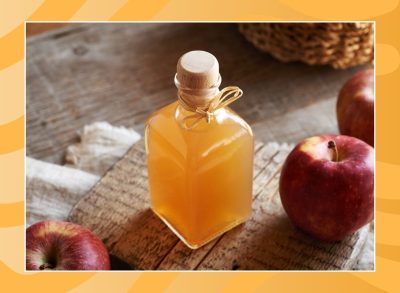 bottle of apple cider vinegar and apples on an orange background