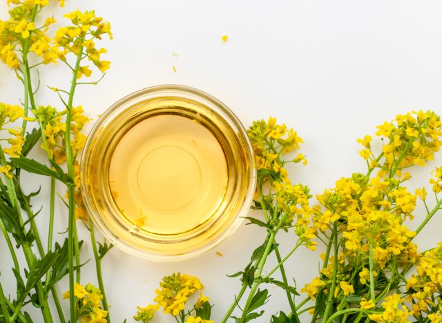 canola oil in a bowl on a flaylay white background surrounded by rapeseed flowers