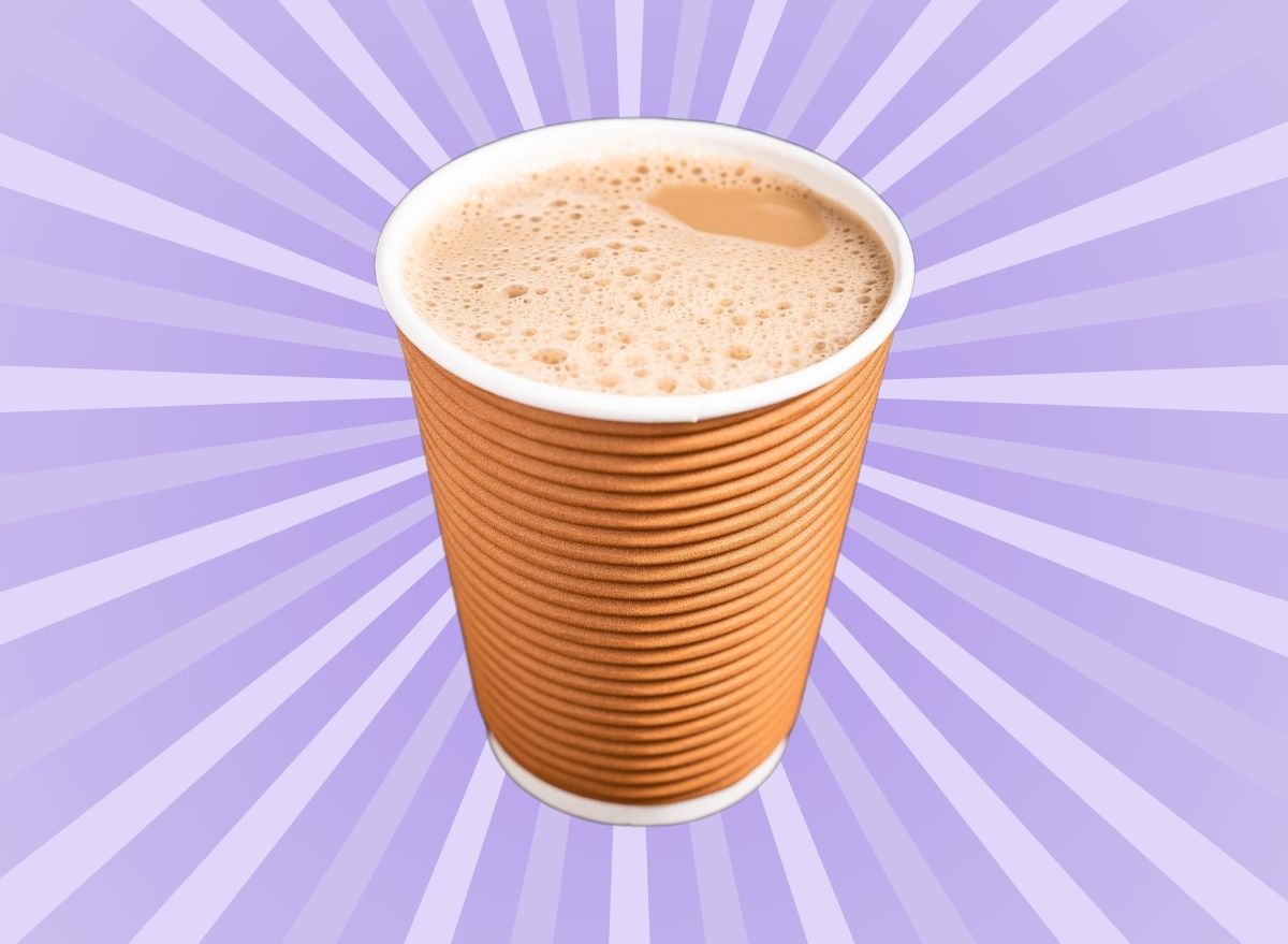 A frothy chai latte in a brown cup set against a vibrant violet background