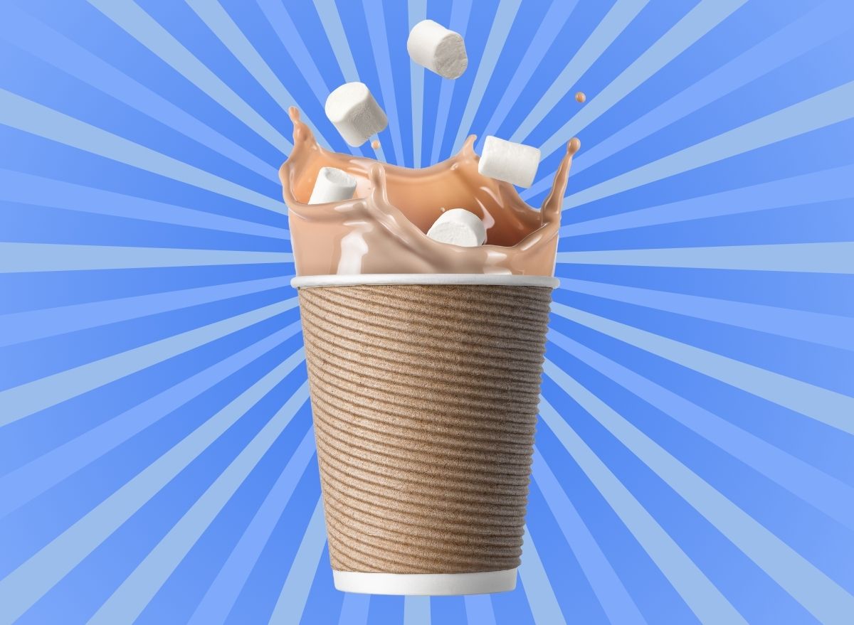 Hot chocolate splashing marshmallows inside a brown paper cup set against a vibrant blue background