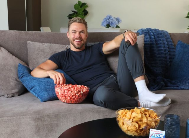 a photo of derek hough on his couch surrounded by bowls of snacks