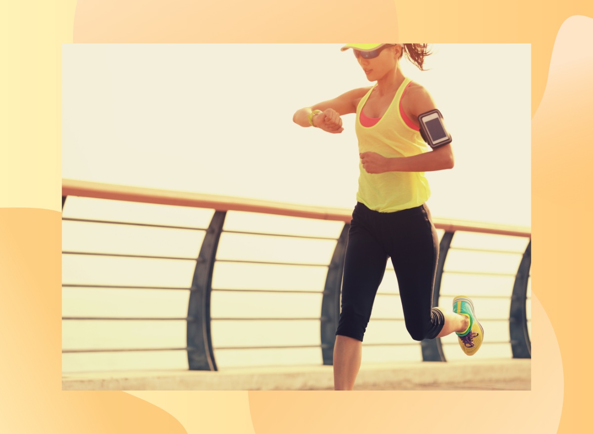 female runner checking heart rate on run along bridge