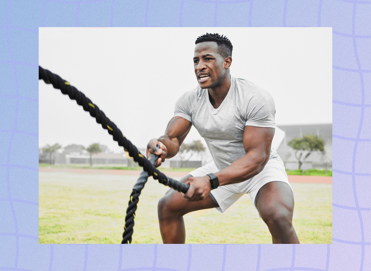 fit, muscular man doing battle rope workout in grassy field