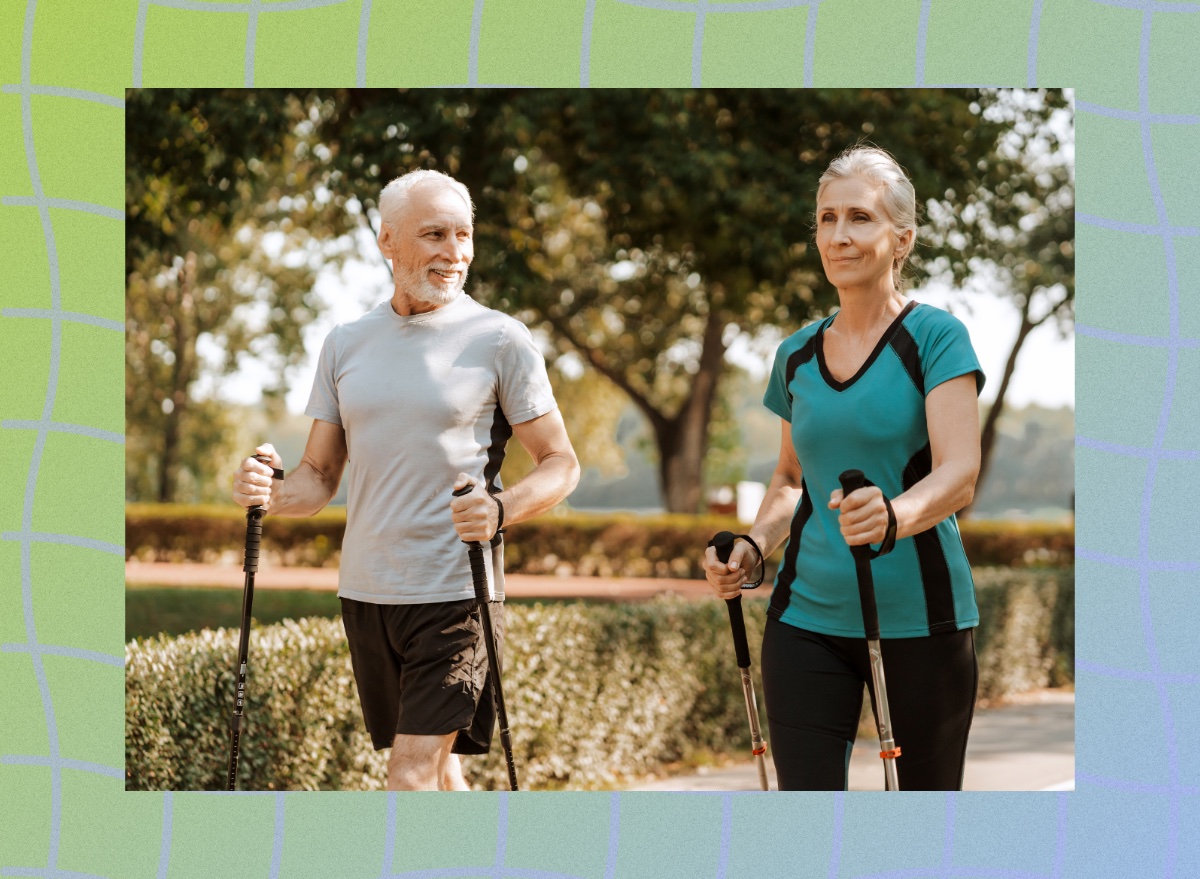 mature couple taking a brisk walk with walking poles along path in park on a sunny day