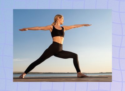 fit, middle-aged woman doing Warrior II yoga pose on mat on a dock by the water at sunset