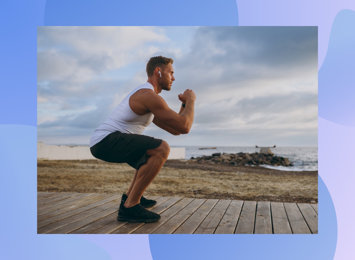 focused, muscular man doing squats on boardwalk leading out to beach on cloudy afternoon