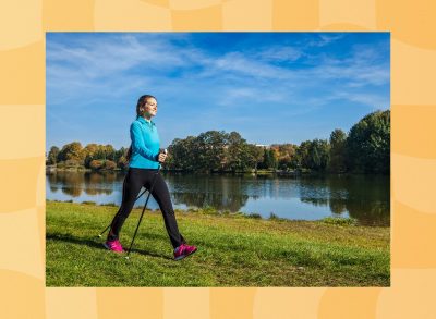 happy young woman doing Nordic walking with walking poles through park by a lake on a sunny day