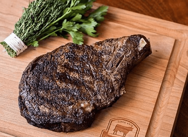 a dry aged ribeye on a cutting board with some herbs