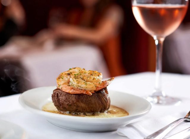 ruth's chris petite filet with shrimp on a plate in front of a glass of wine