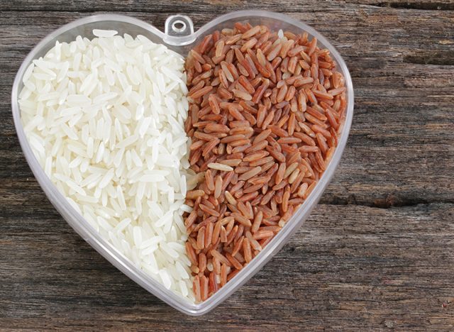 Uncooked basmati rice and brown rice in a plastic bowl on wooded background