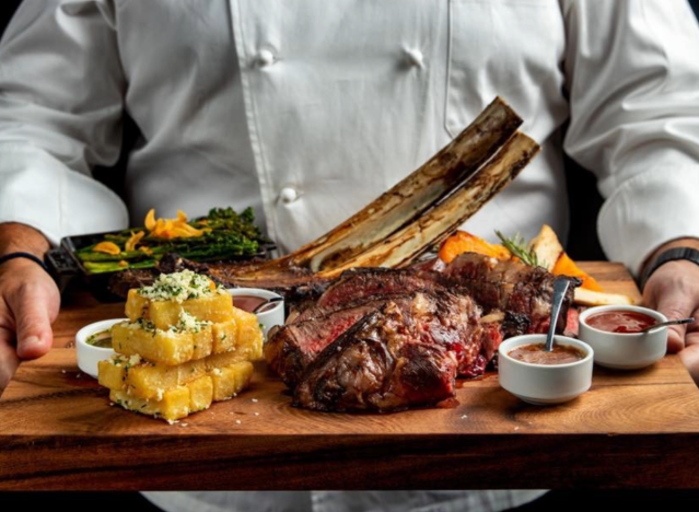 stk dry aged tomahawk on a cutting board bein g held by chef