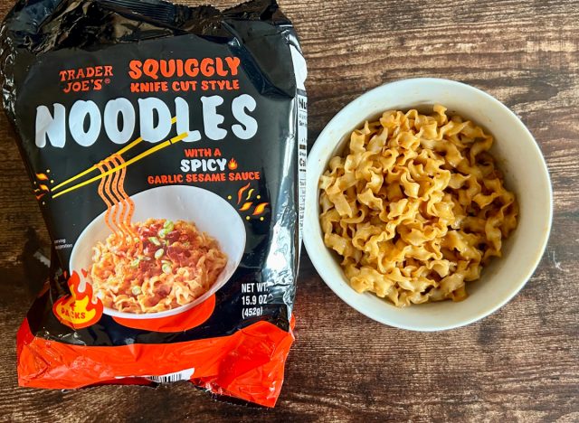 trader joe's squiggly spicy knife cut style noodles in a bowl next to a package of the noodles