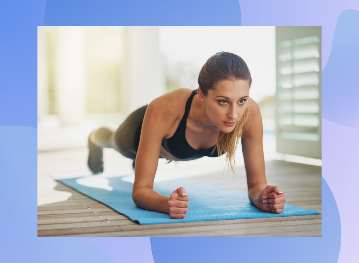 focused woman doing forearm plank on bright blue yoga mat in sunny room