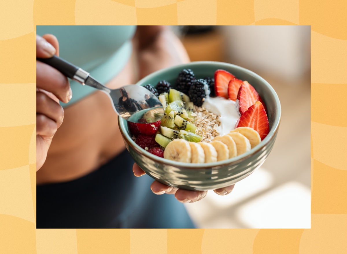 close-up of fitness woman dipping spoon into healthy yogurt bowl with berries and granola