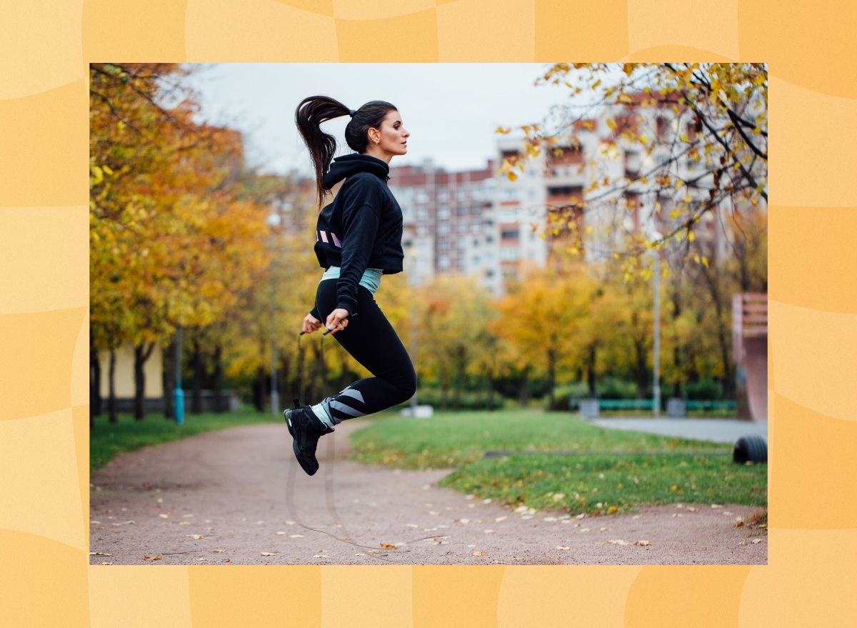 fit brunette woman doing jump rope workout outdoors on autumn day