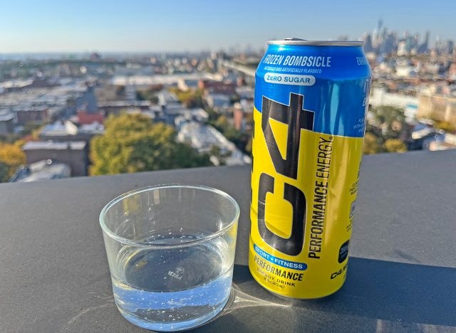 A can of C4 Frozen Bombsicle beside a glass of the energy drink, perched on a rooftop overlooking the NYC skyline.