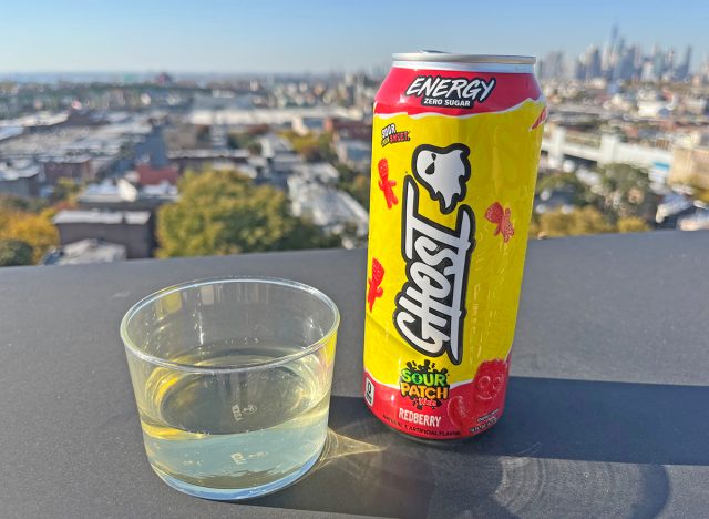 A can of Ghost Sour Patch Kids Redberry beside a glass of the energy drink, perched on a rootfop overlooking the NYC skyline.