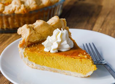 Close-up of a slice of Pumkin Pie on a white plate with fork, and a dollop of cream on the top.