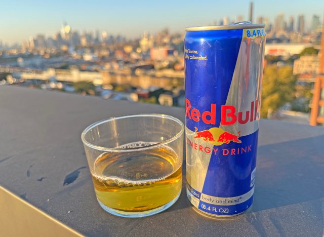 A can of the original Red Bull beside a glass of the energy drink, perched on a rooftop overlooking the NYC skyline.