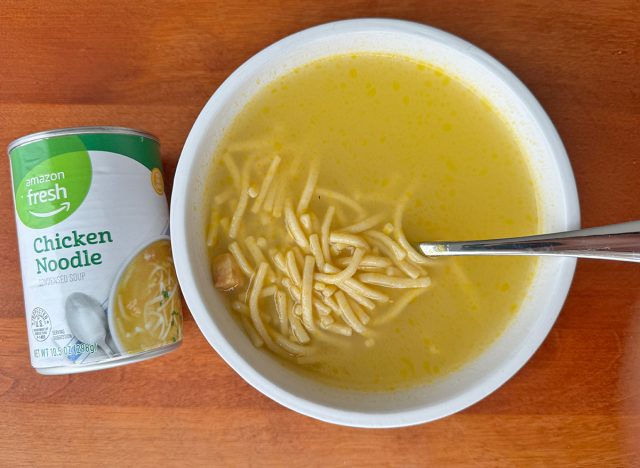 A can of Amazon Fresh Chicken Noodle beside a bowl of the soup