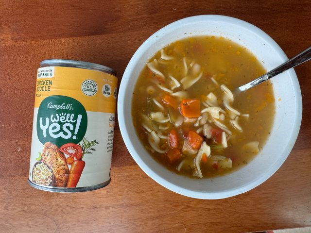 A can of Campbell's Well Yes! Chicken Noodle beside a bowl of the soup