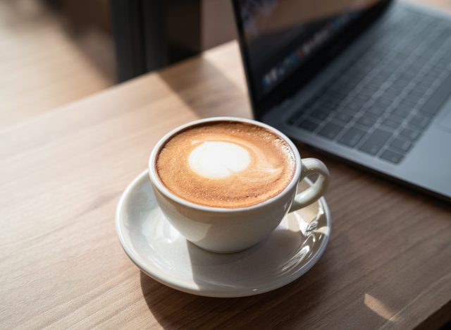 cup of latte on a wooden table next to a laptop