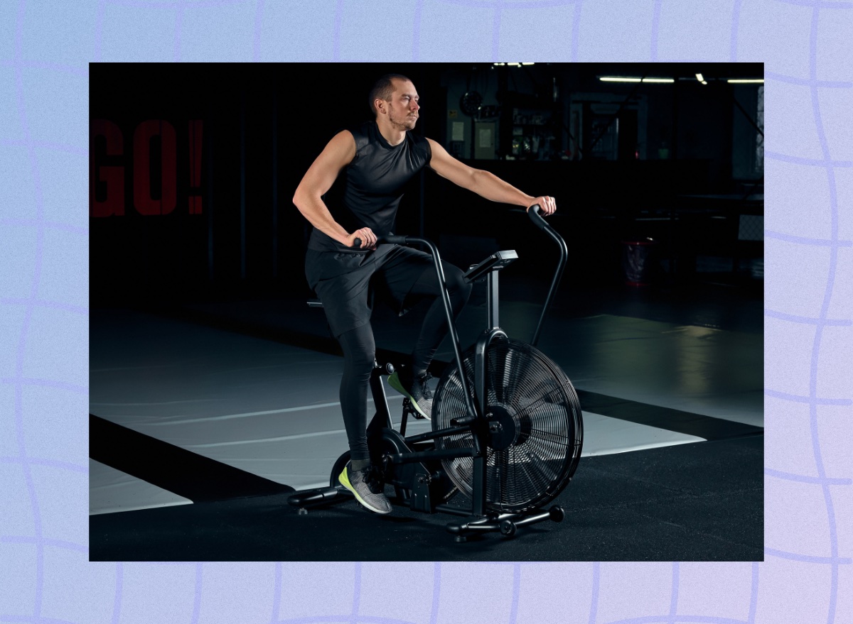 fit, focused man doing an air bike workout in a dark gym setup