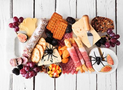 halloween charcuterie board with salami crackers ghost cheese and prosuitto bones on a board with a white table background