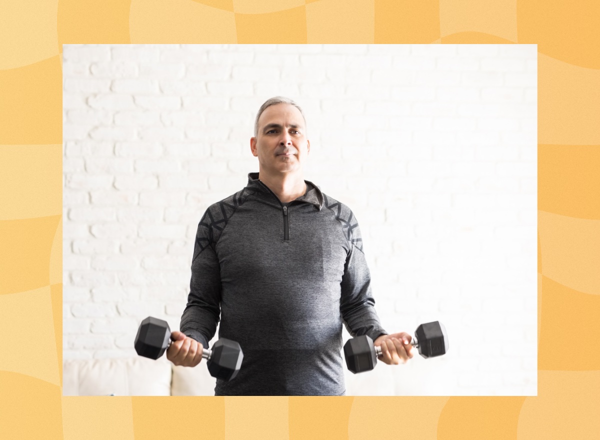 middle-aged man doing a bicep curl exercise with dumbbells in bright living space