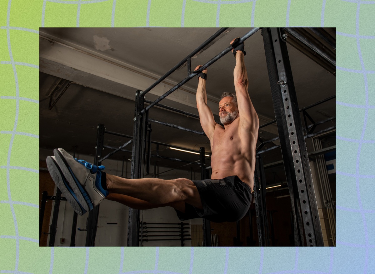 muscular, middle-aged shirtless man doing pull-up exercises in dark gym weight room