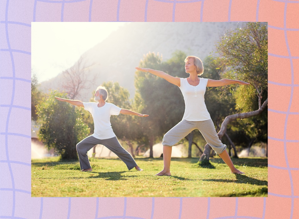 mature couple doing balance yoga exercises in field surrounded by trees on sunny day