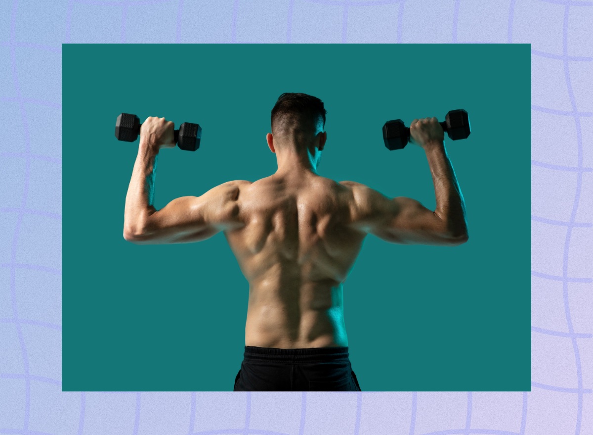 back view of fit, muscular shirtless man doing dumbbell press exercise, lifting dumbbells, in front of greenish blue backdrop