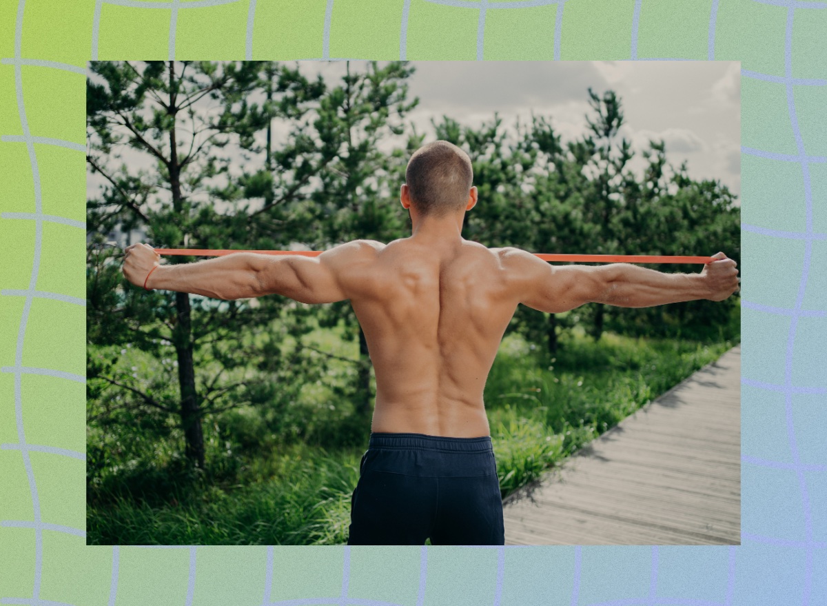 fit, shirtless, muscular man doing a resistance band back exercise outdoors