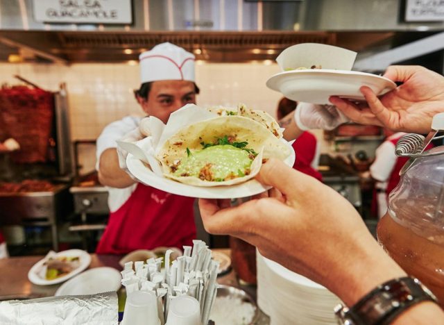 person taking plates of tacos from a Los Tacos No. 1 worker