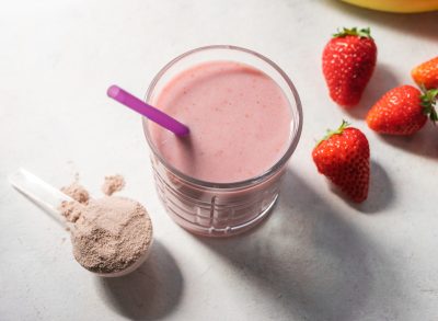 scoop of protein powder next to a strawberry smoothie with whole strawberries