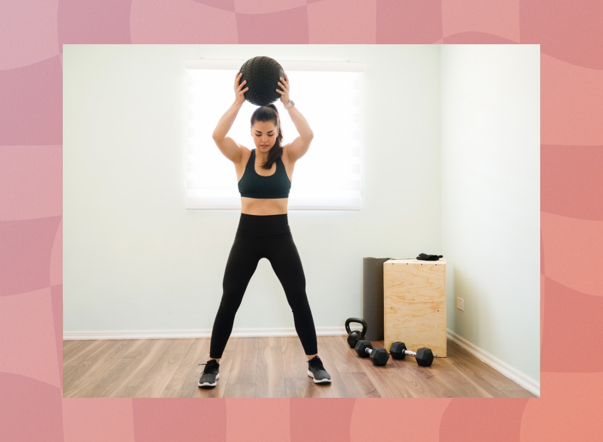 fit, focused woman doing a slam ball front slam exercise in bright workout room