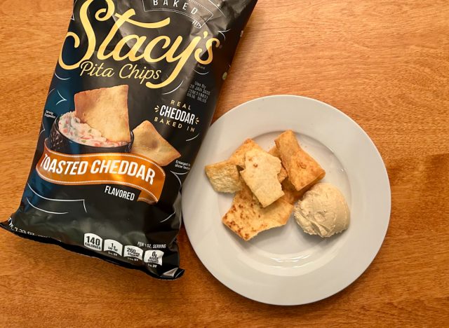 Stacy's Toasted Cheddar pita chips on a plate with hummus next to a bag of the pita chips